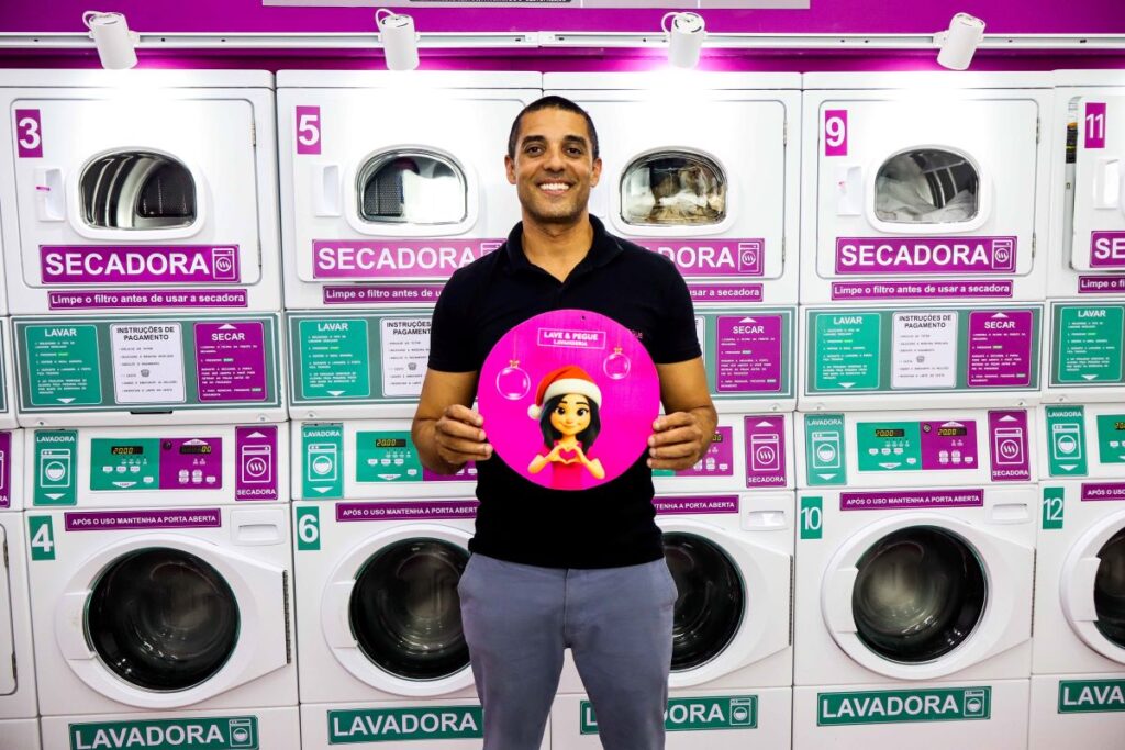Imagem mostra homem em frente à maquinas de lavar industriais exibindo a logo de sua empresa